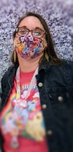 Diana Pomeroy-a person with brown hair and eyes, in a pink MLP tee with a jean jacket, stands against a multicolored background
